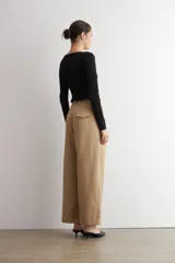 Pantalón pinzado beige de corte ancho y relajado, tiro alto, con bolsillos laterales y detalle de doblez en los bajos.