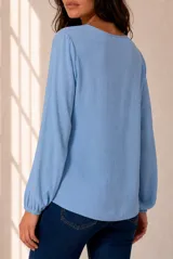 Blusa celeste de manga larga con escote en V y volados en cascada ribeteados en color oscuro. Cuenta con puños elásticos.