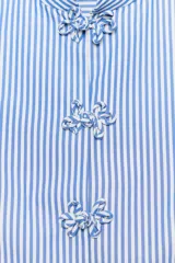 Camisa sin mangas de algodón con rayas verticales blancas y azules, cuello mao, bajo acabado en peplum y cierre frontal con alamares decorativos de nudo.