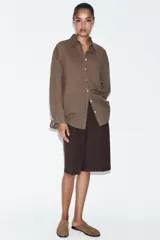 Camisa oversize de algodón con cuello solapa, manga larga y cierre frontal con botones. Presenta un bolsillo de plastrón en el frente y un diseño de corte amplio con ruedo redondeado.