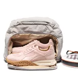 Mochila deportiva color gris, confeccionada en material textil con acabado arrugado. Presenta compartimento principal con cierre doble, bolsillo frontal con logo circular, compartimento inferior independiente para calzado y bolsillos laterales. Incluye tirantes ergonómicos ajustables y espaldera acolchada con malla transpirable.