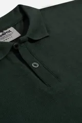 Remera polo de manga larga en tejido piqué, color verde oscuro, con cuello clásico y cierre frontal de dos botones personalizados. Presenta un diseño de ajuste regular.