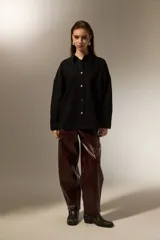 Sobrecamisa de jean color negro, con cierre frontal de botones metálicos, mangas largas y detalle de pequeñas tachas decorativas en la parte superior delantera.