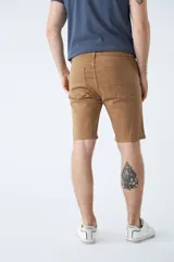 Bermuda clásica de jean color beige, con cinco bolsillos, cierre con cremallera y botón.