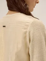 Saco de punto color beige con acabado metalizado, manga larga, cuello redondo y cierre frontal con botones. El diseño combina frente y mangas de tejido abierto con espalda en tela de lino.