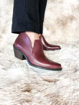 Botín de cuero color bordó, con caña baja, corte en V en el tobillo y taco de madera.