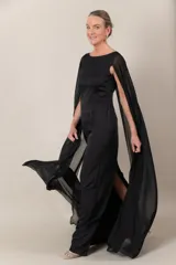 Vestido largo de crepe negro, con capa de gasa que sale de los hombros y abertura en la espalda.