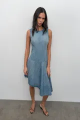 Vestido corto de denim sin mangas con cuello redondo. Presenta costuras marcadas en el cuerpo y un bajo asimétrico con vuelo.
