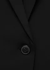 Blazer negro de corte entallado, con cuello de solapa con muesca, hombros estructurados, cierre frontal de un botón, bolsillos de ribete delanteros y manga larga.