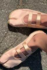 Bailarina de diseño tipo tabi con separación para el dedo, confeccionada en una combinación de gamuza y material textil en tono rosado. Presenta doble tira elástica sobre el empeine, tirador en el talón y suela plana de goma en color tostado.