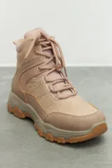 Zapatilla tipo hiking de caña media, confeccionada en una combinación de símil cuero y nylon en tonos beige y rosa suave. Presenta cordones al tono, interior acolchado para mayor abrigo y suela de goma dentada en color marrón con entresuela gris.
