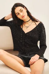 Cardigan negro con escote en V, manga larga y cierre frontal con botones. Presenta un diseño con aplicación de tachas plateadas distribuidas por toda la prenda.