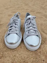 Zapatillas plateadas de cuero con cordones grises y suela blanca.