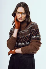 Sweater de punto color marrón, con cuello alto y diseño tejido con patrones geométricos en tonos negros y blancos en la parte superior y mangas.