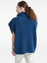 Poncho de punto color azul, con cuello polo y escote en V profundo, sin mangas y diseño holgado.