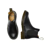 Bota Chelsea Dr. Martens modelo 2976, confeccionada en cuero liso negro con inserciones elásticas laterales, tirador en el talón y suela con cámara de aire reforzada con pespunte amarillo característico.