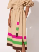 Vestido midi color beige con escote off-shoulder, mangas cortas abullonadas y falda acampanada con estampado de franjas horizontales en colores fucsia, verde y marrón. Incluye cinturón con hebilla.