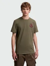 Remera de algodón en color verde oliva, de corte clásico con cuello redondo y manga corta. Presenta un parche bordado con el logo de la marca en el pecho.