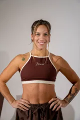 Top deportivo de cuello halter en color marrón chocolate con ribetes en color crema. Presenta el logo de la marca estampado en el centro del pecho.