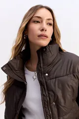Campera puffer de corte cropped, color marrón oscuro, con cuello alto, cierre frontal con cremallera y botones a presión, y puños elásticos.