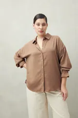 Camisa negra de manga larga con cuello clásico y botones frontales. El tejido presenta una textura arrugada o plisada, y los puños tienen un frunce elástico.