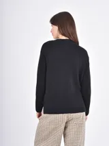 Buzo de tejido de punto color negro, con cuello redondo, mangas largas y puños anchos acanalados. Presenta un diseño con ruedo asimétrico y aberturas laterales.