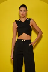 Top negro con diseño cruzado, sin mangas y con botones dorados decorativos en los hombros.