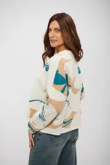 Buzo de tejido de punto con diseño estampado abstracto en tonos beige y turquesa sobre base color crudo, de corte holgado, cuello redondo y mangas largas.