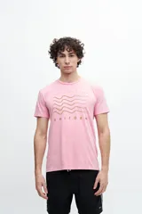 Remera de algodón con efecto desgastado o acid wash, color rojo coral. Presenta un estampado frontal con líneas onduladas en azul marino y el texto "TROPIC TRIBE CREW" y "UNIFORM".