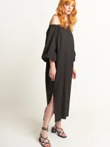 Vestido largo color beige, con escote elastizado que permite usarlo con los hombros descubiertos, mangas largas abullonadas, bolsillos laterales y tajos laterales en el ruedo.