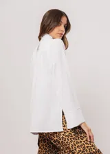 Camisa blanca de cuello redondo con frunces, abotonada y de manga larga con puño abierto.