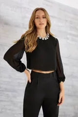 Blusa corta negra de poliéster con mangas largas de gasa abullonadas y cuello redondo. Incluye collar de strass.