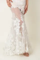 Vestido largo de tul blanco con apliques florales bordados, corte sirena y cuerpo con viso color natural.