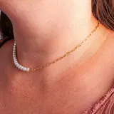 Collar tipo gargantilla con diseño asimétrico, mitad cadena de eslabones dorados y mitad perlas blancas.