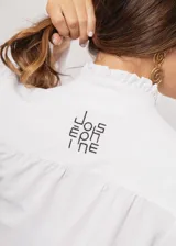 Camisa blanca de cuello redondo con frunces, abotonada y de manga larga con puño abierto.