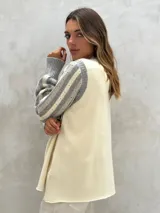 Sweater de lana color crudo con mangas largas abullonadas en gris y blanco, con diseño de rayas y perforaciones. Cuello redondo y puños acanalados.