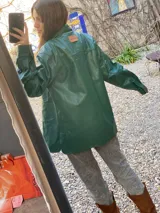 Campera tipo camisa de cuero color verde, con cierre frontal de botones metálicos, cuello clásico y bolsillos frontales con solapa.