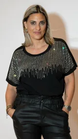 Remera negra de corte amplio con cuello redondo y mangas cortas. Presenta apliques de strass plateados en la parte superior del frente y las mangas.