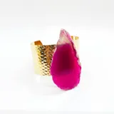 Pulsera dorada tipo brazalete, con textura martillada y una piedra de ágata fucsia.