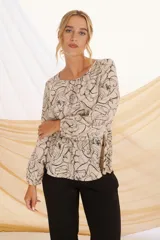 Blusa color crudo con estampado abstracto en negro, de corte holgado, cuello redondo y mangas largas con puños elásticos.