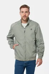 Campera liviana de color verde grisáceo, con cierre frontal, cuello alto y puños elásticos. Presenta un pequeño parche con logo en el pecho.