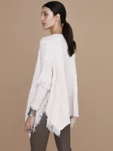 Mantela sweater color crudo, con cuello redondo y mangas largas con flecos. Tejido de punto con diseño de trenzas y bolsillos frontales.