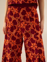 Pantalón de tiro alto y pata ancha con estampado floral en tonos naranja y borgoña. Presenta cintura de tela a tono con abertura lateral con cierre niquelado y tajos en el centro delantero.