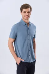 Camisa de piqué lisa color celeste, de manga corta, con cuello camisero y cierre frontal de botones oscuros.