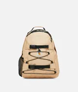 Mochila Carhartt color beige, con sistema de cordones elásticos cruzados en el frente, dos correas ajustables con hebillas de plástico negras y bolsillo lateral de malla negra. Presenta un parche con el logo de Carhartt en el centro.
