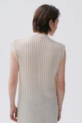 Kimono tejido de punto en color crudo con sutil brillo de lurex. Presenta un diseño sin mangas, corte largo y cierre frontal mediante dos lazos finos. El tejido tiene una textura acanalada vertical.