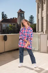 Camisa a cuadros grandes en tonos rosa, blanco y azul. De corte amplio, con cuello clásico, mangas largas con puños abotonados y bajo irregular con aberturas laterales.