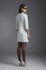 Vestido corto blanco de corte recto, con cuello alto, mangas 3/4 y aplique floral en el hombro.