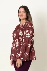 Blusa color marrón con estampado de flores blancas, de manga larga abullonada con puño elástico y cuello redondo con detalle de frunces horizontales.