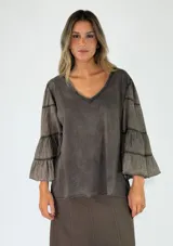 Blusa de algodón color gris oscuro con efecto gastado, mangas largas amplias con múltiples volados escalonados y terminaciones deshilachadas.